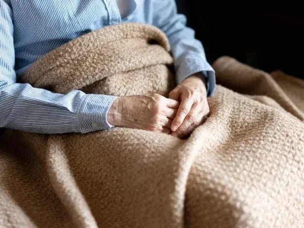 An elderly man cozy and wrapped in blankets