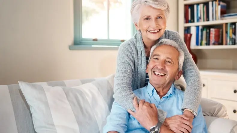 An elderly couple smiling and posing for a photo on the couch